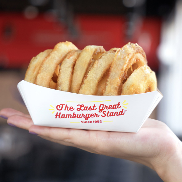 A photo of onion rings in fatburger packaging on someone's hand