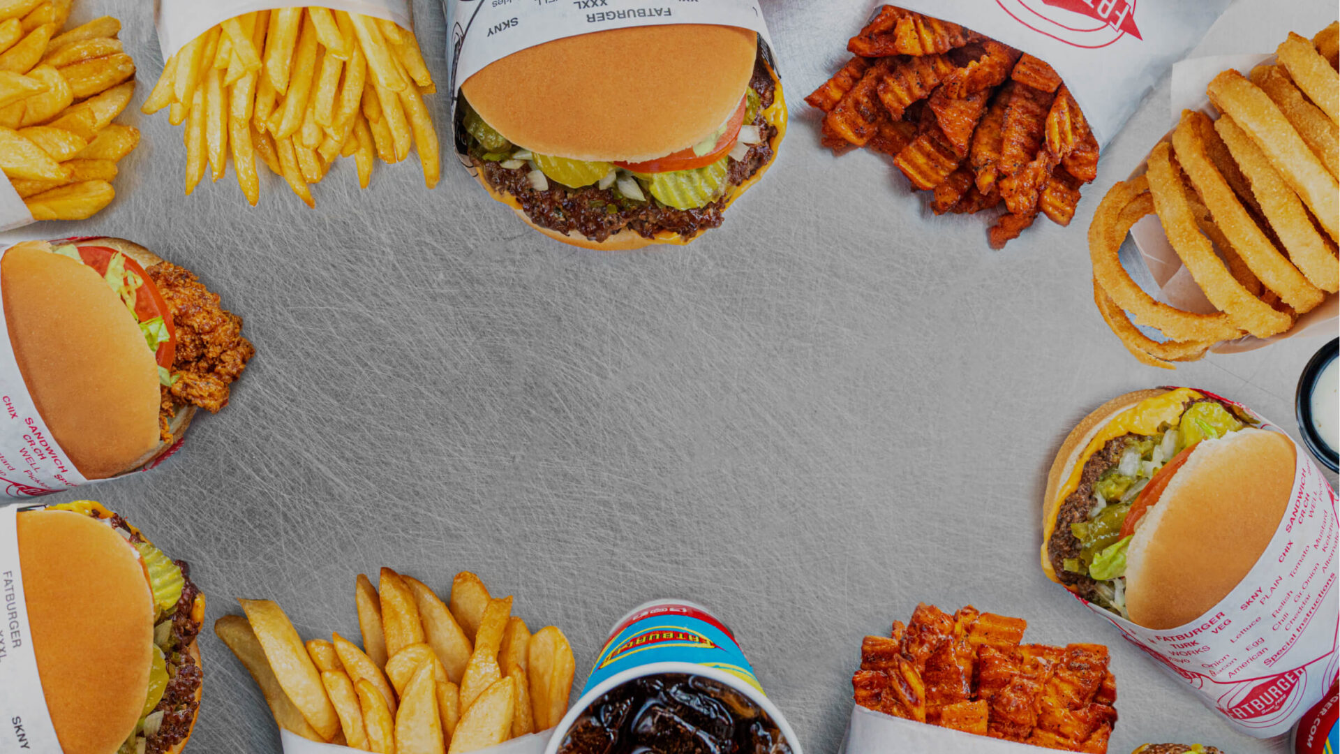 an overhead photo of a collection of fatburgers, onion rings, curly fries, french fries and shakes