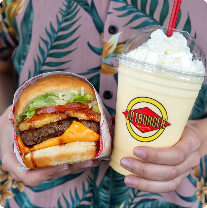 a photo of someone wearing a Hawaiian shirt holding a fatburger and a milkshake
