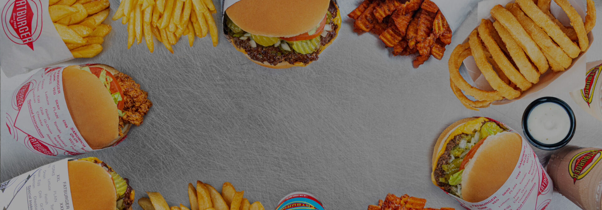 an overhead photo of a collection of fatburgers, onion rings, curly fries, french fries and shakes